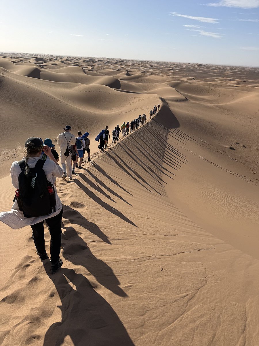 een groep mensen loopt over de rand van een zandduin