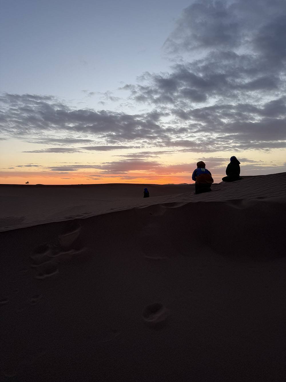 twee mensen zitten in het zand, de zon komt op