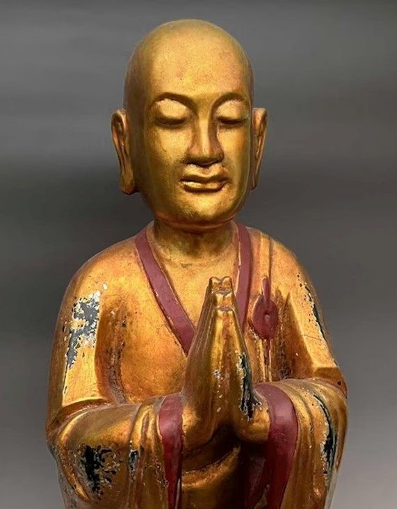 een beeldje van een boeddhistische monnik met de handpalmen tegen elkaar. hier en daar is het goud van het beeldje versleten
