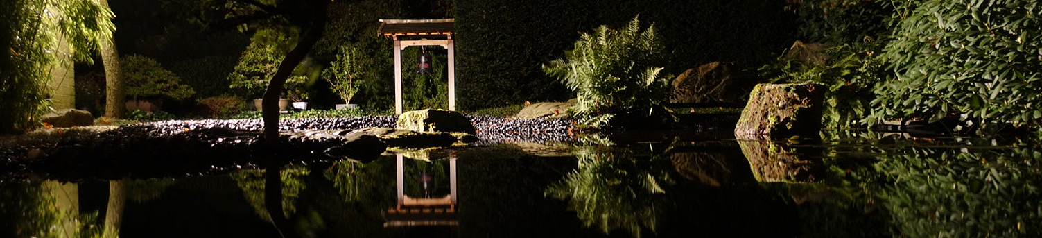 Nachtelijke scene met een natuurlijke vijver. Aan de andere kant van het water valt van achter de bamboe het licht op de tempelbel.