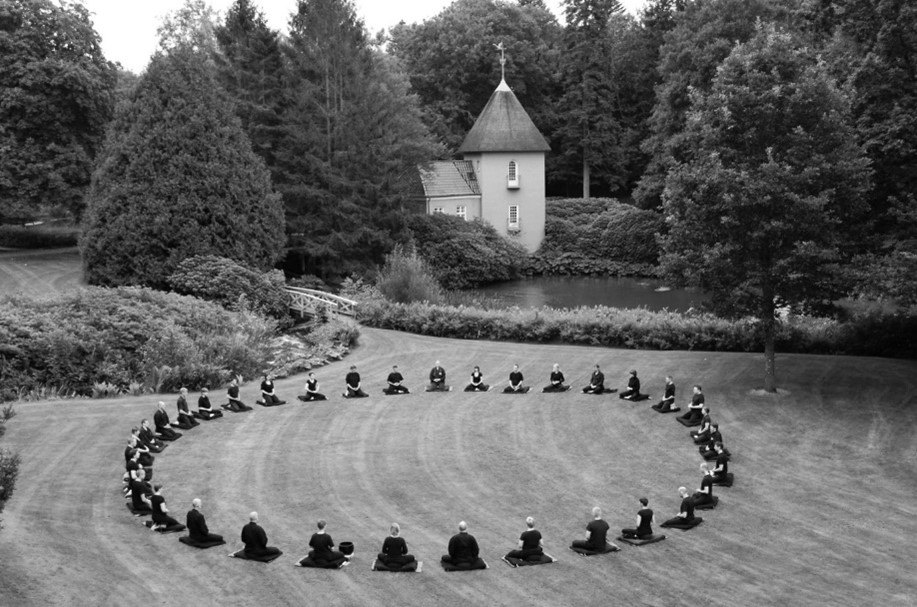 op een grasveld bij een vijver en een kleine toren mediteren de deelnemers aan een sesshins in Denemarken in 2010 in een grote cirkel